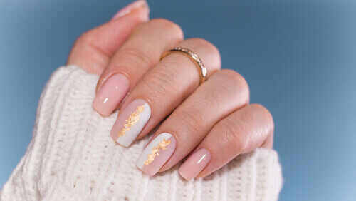 Hand with pink-white nail design with a gold on two nails