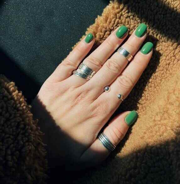 Hand with green nail design on a brown surface